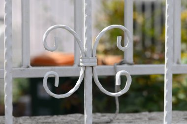 Beyaz bir çitin üzerindeki narin metal parşömen eşsiz desenler oluşturur, yemyeşil ve renkli çiçeklerle güzel tezat oluşturur, doğanın sıcaklığını davet eder..