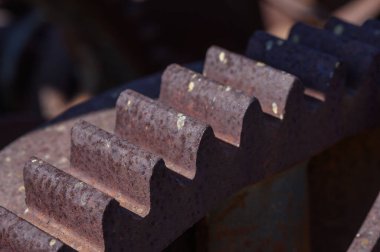 Unutulmuş bir fabrikanın kalıntıları arasında, paslanmış dişlilerin yakın çekimi güneş ışığını yakalar, çürüme ve endüstriyel tarihin güzelliğini gözler önüne serer, zamanın geçişini düşünmeye sevk eder..