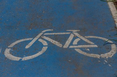 Taze, beyaz bir bisiklet sembolü parlak mavi bir yolda duruyor, bisikletçileri bu şehir ortamında bir yolculuğun tadını çıkarmaya davet ediyor. Güneş ışığı bölgeyi yıkıyor, neşeli atmosferi arttırıyor..