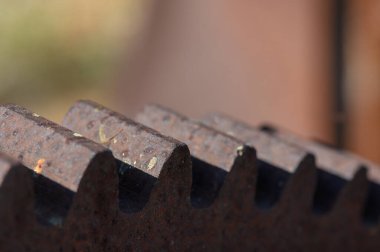 Yakın çekim, metal dişlilerin karmaşık dişlerini yakalar, pas ve dokuyu ön plana çıkarır. Güneş ışığı atölyeyi aydınlatıyor, eski makinelerin güzelliğini ortaya çıkarıyor..