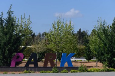 Parlak renkli harfler, açık mavi gökyüzünün altında yemyeşil Park 'ı gösteriyor. Davetkar atmosfer ziyaretçileri gün boyunca doğa ve eğlence faaliyetlerinin keyfini çıkarmaya teşvik ediyor..