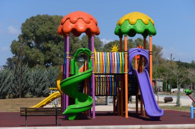 Açık mavi gökyüzünün altında parlak renkli oyun alanı ekipmanları yüksekte duruyor, çocukları tırmanmaya, kaymaya ve eğlenceli özelliklerini keşfetmeye çağırıyor. Renkli yapı açık hava oyun zamanını arttırır.
