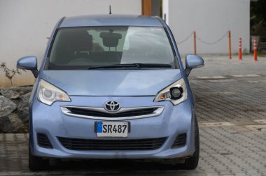 Gaziveren Kıbrıs Rum Kesimi -10.04.2025 Sıkışık mavi bir araç çağdaş bir yapının önünde sessizce duruyor. Açık gökyüzü, park alanının huzurlu atmosferini yükselterek manzarayı aydınlatıyor..