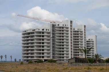 Huzurlu bir manzaranın ortasında, kısmen tamamlanmış, modern bir yerleşim yeri gökyüzüne doğru yükselir. Arka planda kıyı şeridi parıldıyor kasvetli, bulutlu bir gökyüzünün altında.