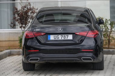 Gaziveren Kıbrıs Rum Kesimi -10.04.2025 modern bir otoparkta parlak kaplamalı şık siyah bir sedan duruyor. Araç, bereketli yeşillik çerçeveli zarif çizgiler ve krom aksanlar sergiliyor..