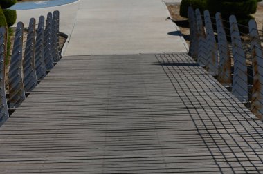 Huzurlu bir parkta huzurlu bir yol üzerinde güzel yapılmış ahşap bir köprü uzanır. Gölgeler, güneşli bir günde sakin yürüyüşler yaparak sahil boyunca zarifçe uzanır..