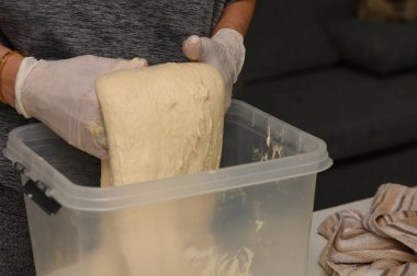 Koruyucu eldivenlere sarılı eller temiz bir konteynırdan yeni yükselen hamuru kaldırıyor. Yumuşak, havadar dokusu, şık bir mutfak ortamında yapılmış ekmek ya da hamur işleri için mükemmel bir temel oluşturuyor..