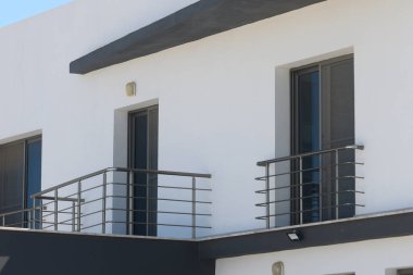 Çağdaş bir binanın çarpıcı manzarası keskin hatlar, zarif balkonlar ve berrak mavi bir gökyüzünün altında parlak bir dış görünüş. Şehir zarafeti modern tasarım elementleriyle buluşur.