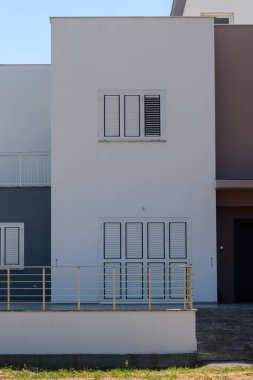 Modern inşaat vitrinleri, açık mavi gökyüzü altında birbiriyle zıt renkler ve mimari basitlikle vurgulanmış canlı bir muhitte zarifçe tasarlanmış dış yapılar sergiliyor..
