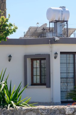 Şık bir evde, çatıdaki yeşil bitkiler ve güneş panelleri tarafından tamamlanmış temiz bir cephe bulunur. Açık mavi gökyüzü, gündüz saatlerinde huzurlu meskun atmosferi güçlendirir..