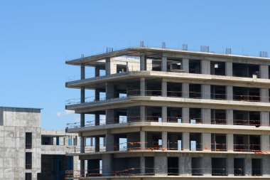 Çalkantılı bir şehrin ortasında, çok katlı bir binanın karmaşık çerçevesini gösteren bir iskelet yapısı yükseliyor. İşçiler, gökyüzü aydınlandıkça vizyonu canlandırmak için bölgede geziniyorlar..