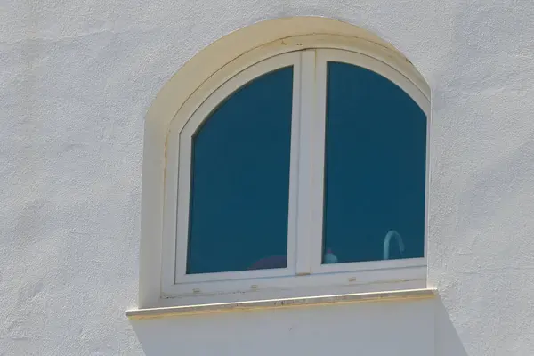 Güzel tasarlanmış kemerli bir pencere parlak güneşi yakalar, berrak camını ve ince detaylarını pürüzsüz beyaz bir duvara doğru gösterir. Sakin öğleden sonra ışığı zarafeti artırır..