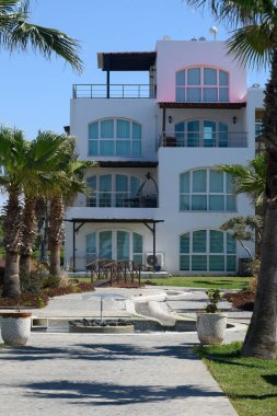 Huzurlu bir sahil inzivası, bereketli palmiye ağaçlarıyla çevrili modern mimariyi gözler önüne seriyor. Büyüleyici bir yürüyüş yolu ziyaretçileri parlak mavi gökyüzünün altındaki davetkar girişe götürüyor..