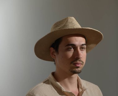 Genç bir adam kendine güvenerek duruyor, özel bir yetenek katan hasır bir şapka takıyor. Düşünceli bakışları, kişiliğini ve karakterini ön plana çıkaran sessiz bir yansıma anı yakalıyor..