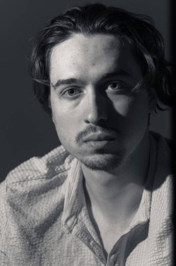 Genç bir adam dikkatlice uzaklığa bakar, gölgeler nazikçe yüzünü okşar. İfadesi bir içgözlem ve sakinlik hissi yayıyor, bir yalnızlık anını vurguluyor..