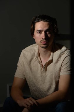 Genç bir adam, alacakaranlıkta sakin bir atmosferle sarmalanan mesafeye bakarken gölgelerin arasında nazikçe oturuyor..