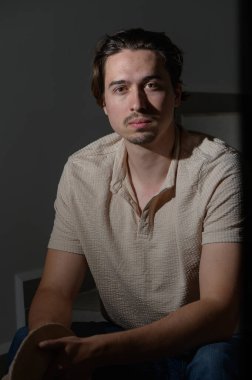 Genç bir adam, hafifçe aydınlatılmış bir odada oturuyor. Direk karşıya bakarken yüzündeki o düşünceli ifade. Sıcak ortam, onun yansıma anını geliştiren samimi bir atmosfer yaratıyor..