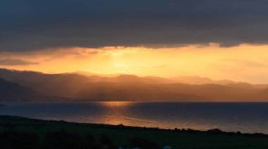 Güneş uzak dağların ardında batarken nefes kesici bir manzara beliriyor. Sakin sulara altın ışınlar saçıyor ve manzarayı sıcak renklerle kaplıyor..