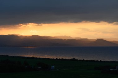 Akşam yaklaşırken, zengin turuncu ve altın gölgeleri dağların tepelerine dökülüyor. Sakin deniz çarpıcı gökyüzünü yansıtıyor ve bu gizli cennette sakin bir atmosfer yaratıyor..
