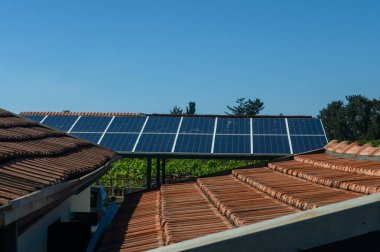 Çatı katlarındaki güneş panelleri güneş ışığını yakalayarak sakin bir köy ortamında yeşil enerjiyi teşvik ediyor. Canlı mavi gökyüzü manzaranın çevre dostu atmosferini arttırır..