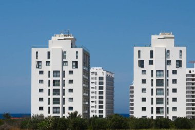 Kıyı şeridi boyunca güneş ışığını yansıtan iki çağdaş beyaz yerleşim yeri ayakta duruyor. Yeşilliğin etrafını sarmak sakin atmosferi güçlendirir, deniz kenarı için davetkar bir çekilme yeri haline getirir..