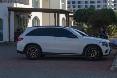 Gaziveren Kıbrıs Rum Kesimi -16.04.2025 Şık beyaz bir SUV lüks bir konut ortamında modern mimarinin bir zeminine park edildi.