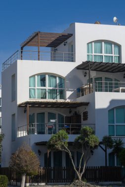 Gösterişli, modern bir bina canlı mavi gökyüzüne karşı gururla duruyor büyüleyici balkonları ve yeşil pencereleri davetkar bir atmosfer yaratıyor..