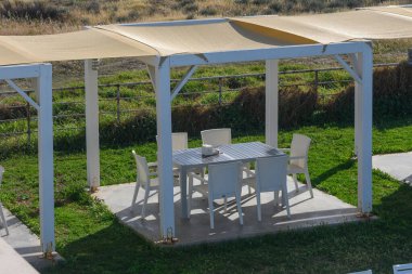 Samimi bir açık hava yemek düzeninde, güneşliğin altına yerleştirilmiş, sandalyelerle çevrili şık bir masa bulunur. Bereketli yeşil çimenler, dingin atmosfere katkı sağlar. Toplamak için birebir..