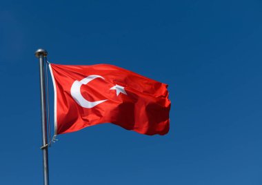 Canlı bir halk meydanında, Türk bayrağı açık mavi gökyüzü altında ulusal gurur ve birliği simgeleyen meltemde zarifçe dalgalanıyor. Sahne kültürel öneme sahip bir anı yakalıyor..