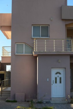 Çağdaş pembe bir evde kendine özgü mimari özellikleri, güneş ışığını yansıtan geniş pencereleri ve hoş geldin kapısı bulunur..