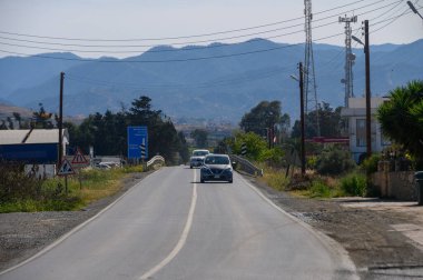 Parlak mavi bir gökyüzünün altındaki görkemli dağlarla çevrili, yemyeşil ve yuvarlanan tepelerle çevrili, dolambaçlı bir yolda araçlar geziniyor. Huzurlu kırsal titreşimler yayılıyor.