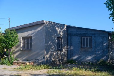 Sakin bir kırsal alanda, berrak mavi gökyüzünün altında yıpranmış bir bina duruyor. Aşırı büyümüş çimenler ve narin çiçekler dokulu duvarlarının etrafını sarmış. Geçmişe dair hikayeler anlatıyorlar..