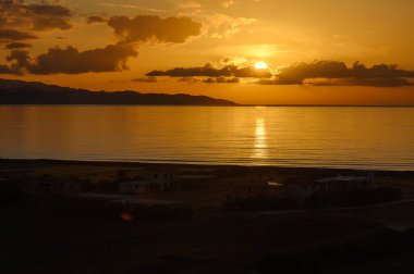 Güneş ufukta dinlenirken, altın renkler gökyüzüne ve suya yayıldı, dingin manzarayı aydınlattı. Huzurlu bir an, kıyı cennetinde günün sonunu yakalar..