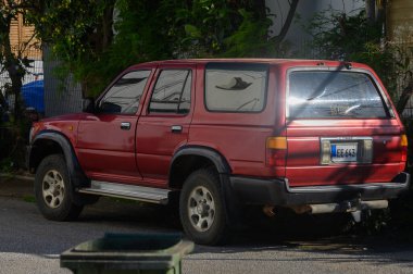 Parlak bir gökyüzünün altında, yeşil yollarla çevrili, çarpıcı kırmızı bir SUV yer alır..
