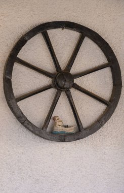 Kırsal ahşap bir tekerlek desenli bir duvara asılır, merkezinde büyüleyici bir ayakkabı figürü sergilenir. Bu eşsiz el işi ve sanat karışımı ilgi çekici detaylarıyla dikkatleri çeker..