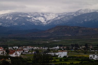 Karla kaplı zirveler bulutlu bir günde beyaz ve kırmızı çatılı evlerle dolu sakin bir köyün üzerinde görkemli bir şekilde yükselir..