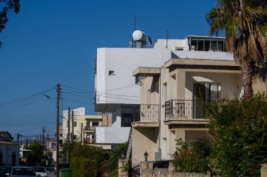 Kıbrıs 'ta sakin bir mahalleyi aydınlatan parlak güneş ışığı, klasik mimarinin yanında parlak çizgileri olan modern binalar sergiliyor. Bereketli yeşillik manzaraya sakinleştirici bir dokunuş ekler..