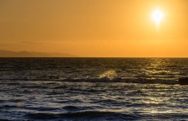 Bir grup arkadaş kumlu bir plajda toplanıyor, gülüyor ve özenle hazırlanmış bir kumdan kale yapmak için birlikte çalışıyorlar. Bazıları dalgalarda oynarken, diğerleri dekorasyonlara yardım ediyor..
