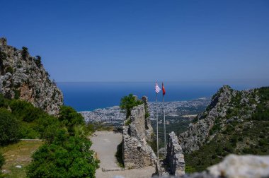 St. Hilarion Şatosu 'nda dalgalanan Türkiye ve Kuzey Kıbrıs bayrakları, antik taş duvarların zeminine karşı kültür mirası ve tarihi simgeliyor..