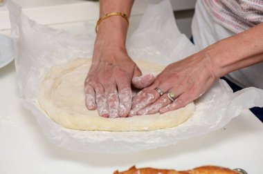 Kadın sıcak bir mutfakta ev yapımı pizza hazırlıyor. Yuvarlanan hamurlar, malzemeler ve sevgi ve özenle taze bir yemek yaratmak. Ev yemeği konsepti.