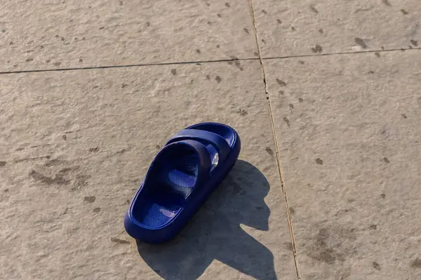 Güneşli bir günde, ıslak zeminde uzanan mavi bir parmak arası terlik yazı ve rahatlamayı simgeliyor..