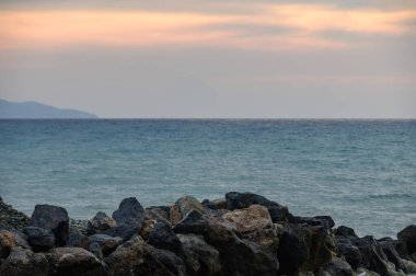 Sakin Akdeniz ve Kıbrıs kıyılarındaki uzak dağlar üzerinde ılık bir altın saat ışığı. Doğal güzelliği ve rahatlatıcı atmosferi olan manzaralı kıyı manzarası.