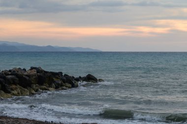 Altın gün batımı ışığı Akdeniz 'i ve Kıbrıs' ın dağ kıyı şeridini aydınlatıyor. Huzurlu bir atmosferi olan sakin deniz manzarası, seyahat ve doğa temaları için ideal..