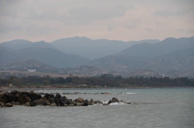 Kıbrıs 'ın Akdeniz kıyısında sakin bir sahilin akşam manzarası sakin bir deniz ve alacakaranlık altında uzak dağlar. Huzurlu doğa ve seyahat manzarası.