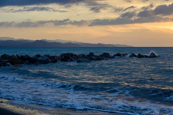 Sıcak altın güneş ışığı, gün batımında Kıbrıs 'ın kayalık kıyılarını aydınlatıyor. Sakin dalgalar, parlayan gökyüzü ve deniz kenarındaki sakin ada atmosferi..