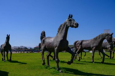 Üniversite binalarının önünde bronz at heykelleri ve yakınlarda bir cami. Kuzey Kıbrıs 'ta barışçıl kültür manzarası.