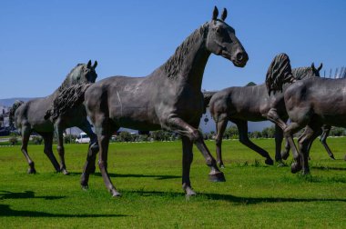 Kuzey Kıbrıs 'taki cami ve akademik binaların yakınlarındaki yeşil çimlerde bronz at heykelleri. Kültürel ve manzaralı görüş.
