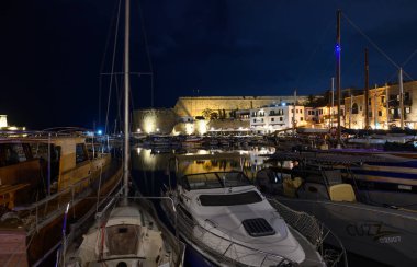 Aydınlanmış Kyrenia kalesi geceleri sakin limanın üzerinde duruyor. Kuzey Kıbrıs 'tan tekneler ve parlayan mimariyle huzurlu bir manzara.