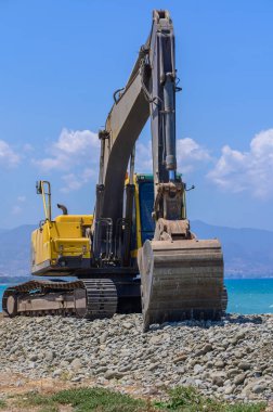 Sarı bir kazıcı Kıbrıs 'taki bir sahildeki kumu düzleştiriyor. Akdeniz yakınlarında açık mavi gökyüzü altında inşaat veya bakım çalışmaları.