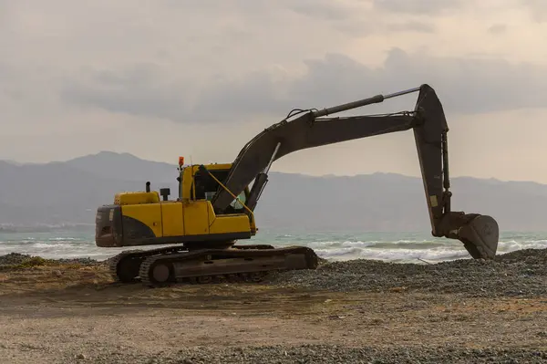 Kıbrıs 'ta kumlu bir sahilde sarı kazıcı, mavi Akdeniz suları yakınında çalışıyor..